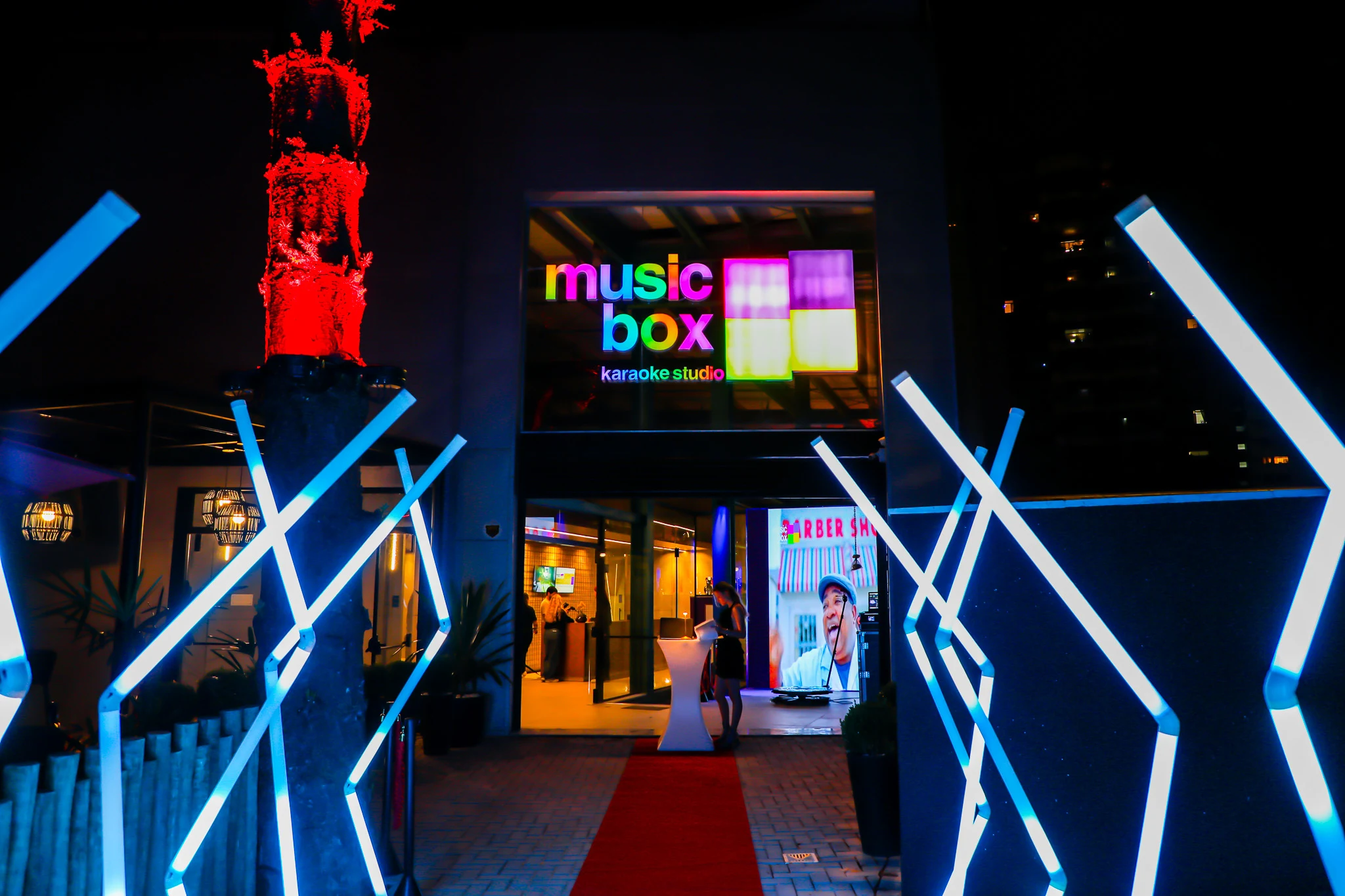 Fachada de entrada do Music Box Karaokê Studio iluminada à noite, referência para chegar ao local